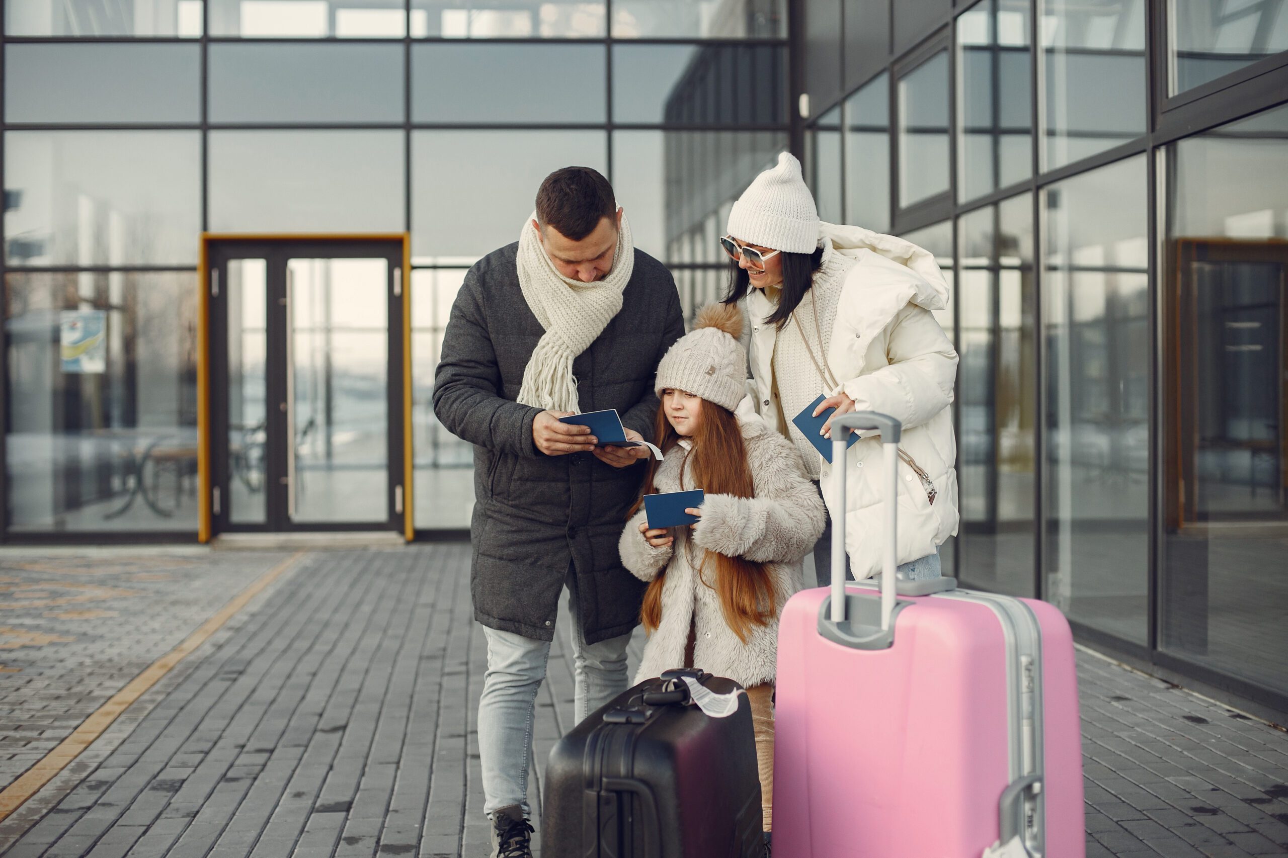 a man and woman standing outside with luggage and a girl looking at a tablet